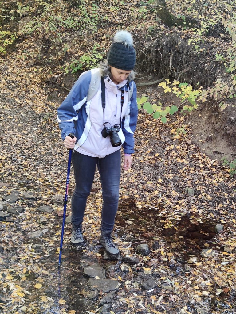 kiránduló nő átkel a patakon csúszós köveken